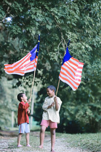 Boys holding malaysian flags while standing against trees in park