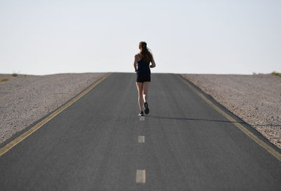 Rear view of woman walking on road against clear sky