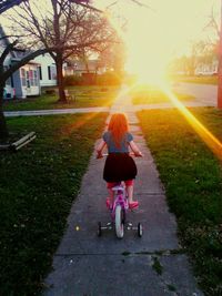 Rear view of girl riding bicycle on footpath during sunset