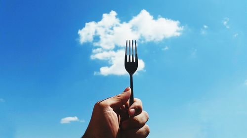 Close-up of hand holding ice cream against blue sky