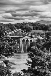 Menai bridge over river against cloudy sky