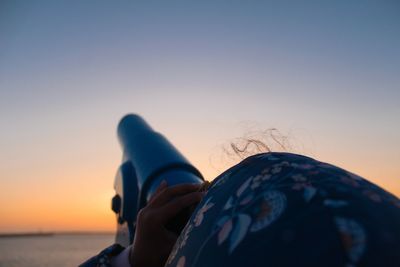 Close-up of woman looking through telescope against sky during sunset
