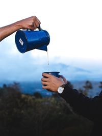 Midsection of person holding bottle against sky