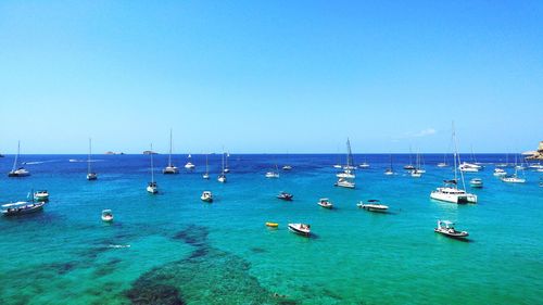 Boats moored on sea against clear blue sky