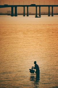 Silhouette man standing in sea during sunset