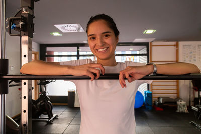 Happy hispanic young woman leaning on a barbell at the gym
