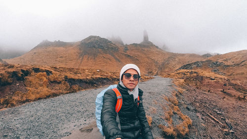 Portrait of young man standing on mountain against sky