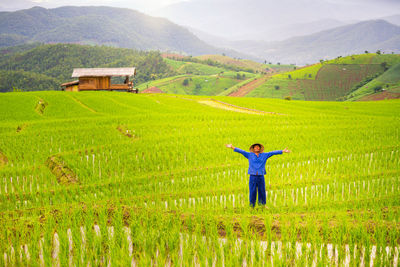 Full length of farmer with arms raised standing at farm