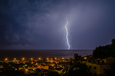 Lightning over illuminated cityscape against sky at night