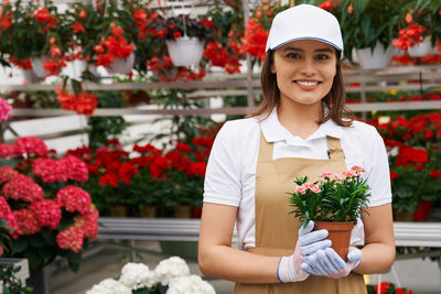 Portrait of young smiling florist holding flowering plants