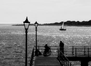 Silhouette people on railing against sea against clear sky