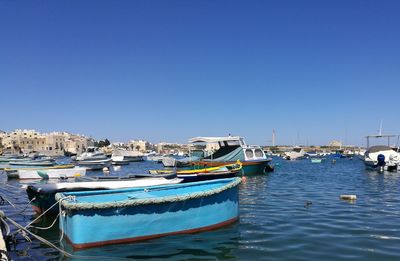 Boats moored at harbor against clear blue sky