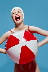 Portrait of young woman with arms raised standing against blue background