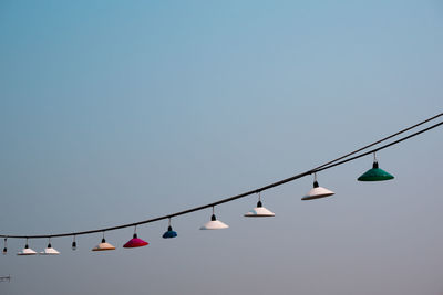 Low angle view of light bulbs hanging against clear sky