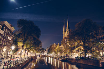 Canal in illuminated city by church against sky at night