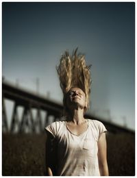 Young woman tossing long blond hair against sky