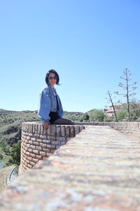 Woman sitting on railroad track against clear blue sky