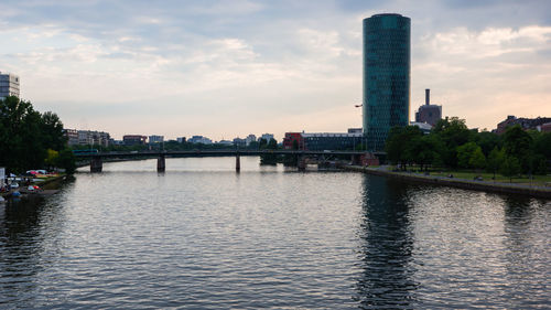 Bridge over river by buildings against sky during sunset