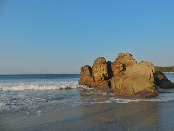 Rock formations at beach against clear blue sky