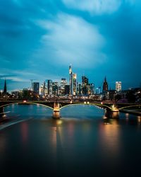 Illuminated bridge over river by buildings against sky in city