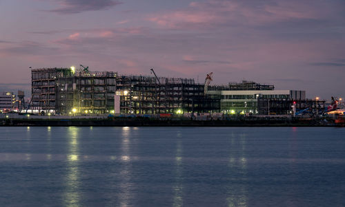 Illuminated buildings by sea against sky at night