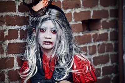 Portrait of girl with spooky make-up standing by brick wall during halloween