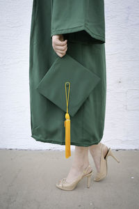 Low section of woman holding mortarboard while standing on footpath