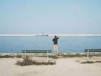 Rear view of man standing by sea against clear sky