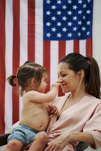 A young woman sitting with her daughter with the american flag in the background. 