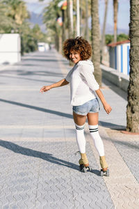 Rear view portrait of woman roller skating on sidewalk in city