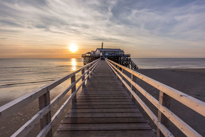 Pier over sea against sky during sunset