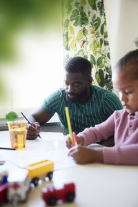 Father and daughter drawing while sitting at dining table