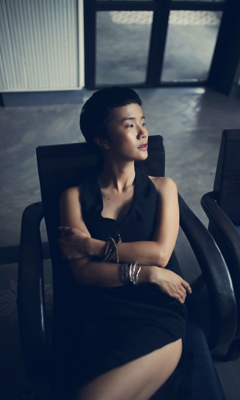 YOUNG WOMAN LOOKING AWAY WHILE SITTING IN CORRIDOR