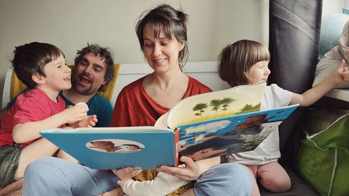 Happy parents reading a book to children sitting in the bed