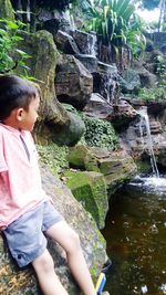 Rear view of boy on rock at waterfall