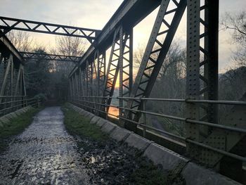 Metallic bridge over river against sky during sunset