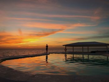 Silhouette people standing by swimming pool against sky during sunset