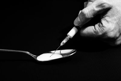 Cropped hand injecting chemical on spoon against black background