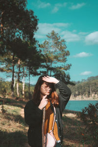 Woman wearing hat standing by tree against sky