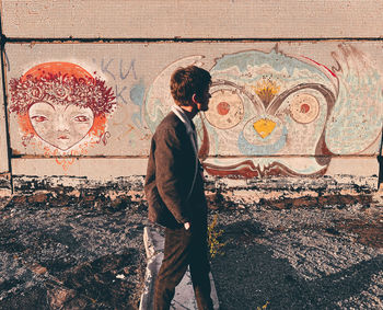 Side view of man standing against graffiti wall