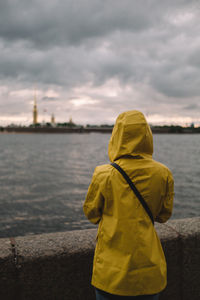 Woman traveler in yellow raincoat looking forward on dramatic landscape. 