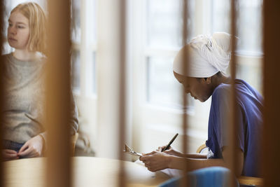 Female doctor sitting and writing notes, teenage patient in background