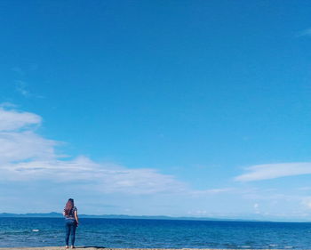 Rear view of woman standing by sea against sky