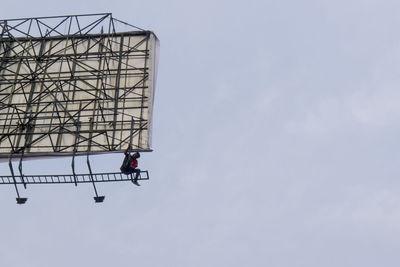 Low angle view of man working on billboard against sky