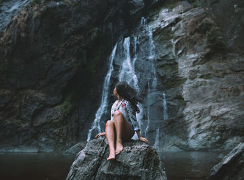 Woman sitting on rock against waterfall