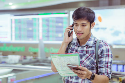 Young man talking on phone while holding map at airport