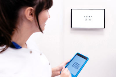 Cropped unrecognizable female optometrist examining eyesight of patient with digital test chart during visit in modern clinic