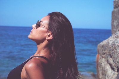 Young woman wearing sunglasses against sea against sky