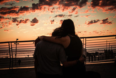 Woman standing by railing against orange sky