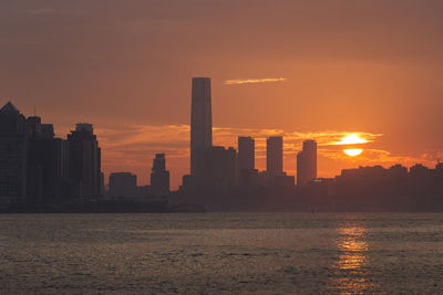 Silhouette buildings by sea against sky during sunset